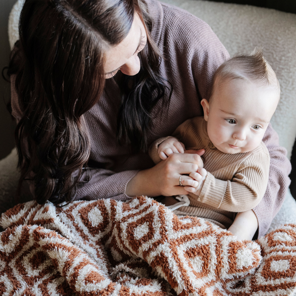 A mother, her little boy, and a double-layer Bamboni® baby blanket. The plush, breathable blanket featuring a chic burnt orange and cream geometric pattern, offering ultimate softness and warmth. Made from Saranoni’s signature stretchy, cloud-like Bamboni® fabric, this luxury baby blanket provides comfort for naps, tummy time, and on-the-go snuggles. The soft blanket is a luxury blanket and Saranoni blanket. 