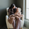 A mother holds her little boy and a double-layer Bamboni® baby blanket. The plush, breathable blanket featuring a chic burnt orange and cream geometric pattern, offering ultimate softness and warmth. Made from Saranoni’s signature stretchy, cloud-like Bamboni® fabric, this luxury baby blanket provides comfort for naps, tummy time, and on-the-go snuggles. The soft blanket is a receiving blanket and Saranoni blanket. 