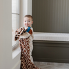 A little boy holds a double-layer Bamboni® baby blanket. The plush, breathable blanket featuring a chic burnt orange and cream geometric pattern, offering ultimate softness and warmth. Made from Saranoni’s signature stretchy, cloud-like Bamboni® fabric, this luxury baby blanket provides comfort for naps, tummy time, and on-the-go snuggles. The soft blanket is a receiving blanket and Saranoni blanket. 