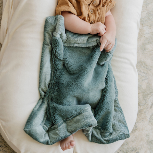 A newborn sleeps under a Eucalyptus colored Lush Saranoni Blanket. The soft blanket is a small blanket and a baby blanket.