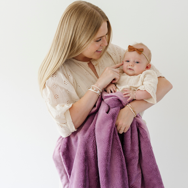 A mother holds her little girl in a Luxury Receiving Fairy Wings (light pink purple) Colored Lush Saranoni Blanket. The soft blanket is a small blanket and a baby blanket or toddler blanket.