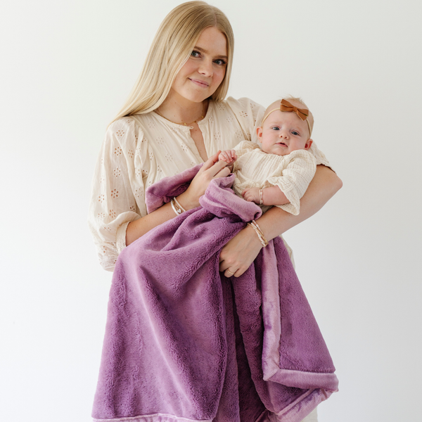 A mother holds her little girl in a Luxury Receiving Fairy Wings (light pink purple) Colored Lush Saranoni Blanket. The soft blanket is a small blanket and a baby blanket or toddler blanket.