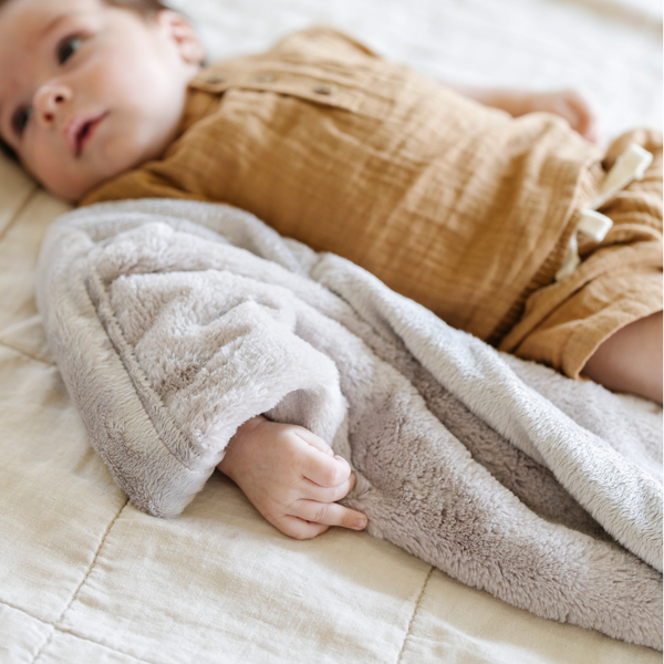 A Little Baby boy hugging a Mini Saranoni Lush baby Blanket that is Feather Colored (similar to a light tan).