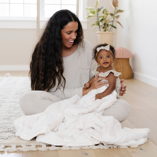 A mother sits with her little girl with a Luxury Receiving Natural (off-white) Colored Lush Saranoni Blanket. The soft blanket is a small blanket and a baby blanket or toddler blanket.