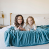 Two little girls smile with a Mineral Blue Lush XL Saranoni blanket, designed for oversized comfort and featuring a buttery soft, plush texture. This luxurious Saranoni blanket is perfect for cozy evenings, reading, or home decor. The Saranoni blanket adds warmth, style, and unmatched softness, making it an ideal gift or essential for ultimate relaxation. The soft blanket is a luxury blanket and a Saranoni blanket. 