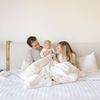 A husband, wife, and their little girl sit with a Natural (cream) Lush XL Saranoni blanket, designed for oversized comfort and featuring a buttery soft, plush texture. This luxurious Saranoni blanket is perfect for cozy evenings, reading, or home decor. The Saranoni blanket adds warmth, style, and unmatched softness, making it an ideal gift or essential for ultimate relaxation. The soft blanket is a luxury blanket and a Saranoni blanket. 