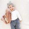 A baby girl lays with a mini blanket that is a dusty peach colored blanket. The soft blanket is a lush blanket and a baby blanket as well as a Saranoni blanket. This cozy blanket is a luxury blanket for babies and is so soft. 