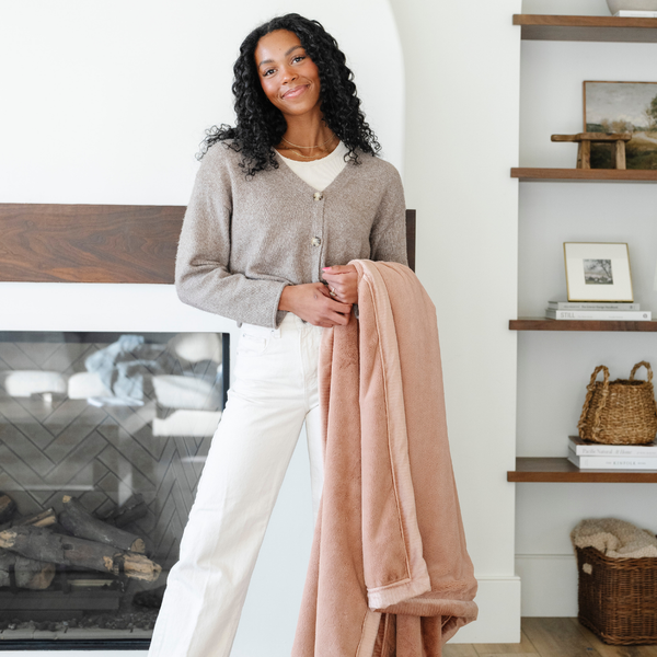 A woman holds a Rosy (dusty peach) Lush XL Saranoni blanket, designed for oversized comfort and featuring a buttery soft, plush texture. This luxurious Saranoni blanket is perfect for cozy evenings, reading, or home decor. The Saranoni blanket adds warmth, style, and unmatched softness, making it an ideal gift or essential for ultimate relaxation. The soft blanket is a luxury blanket and a Saranoni blanket. 