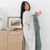 A woman holding a green and white Saranoni XL muslin quilt in a soft geometric print. This luxury blanket features four layers of ultra-soft bamboo muslin, creating an airy yet cozy feel. Designed with a stitched quilted pattern and a one-inch border, this breathable blanket is perfect for muslin lovers looking for extra warmth and comfort. Made from bamboo fabric, this soft muslin quilt is a lightweight quilt that offers a cozy, home décor accent. The softest blanket and a Saranoni blanket. 