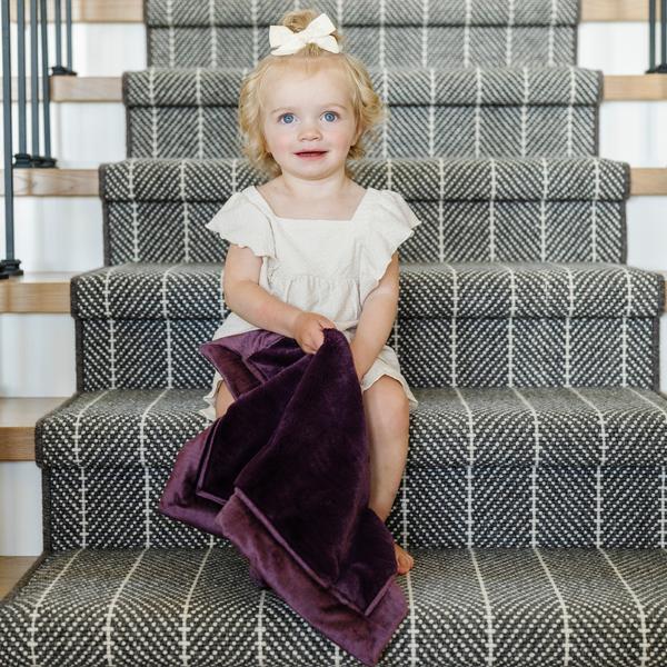 A little girl holds a Mini Aubergine (deep purple) Colored Lush Saranoni Blanket. The soft blanket is a small blanket and a baby blanket.