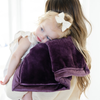 A mother holds her little girl who is laying on a Mini Aubergine (deep purple) Colored Lush Saranoni Blanket. The soft blanket is a small blanket and a baby blanket or toddler blanket.