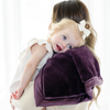 A mother holds her little girl who is laying on a Mini Aubergine (deep purple) Colored Lush Saranoni Blanket. The soft blanket is a small blanket and a baby blanket or toddler blanket.