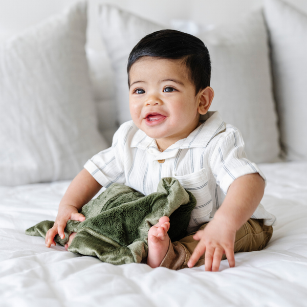 A baby boy holds a Mini Fern Colored Lush Saranoni Blanket. The soft blanket is a small blanket and a baby blanket.