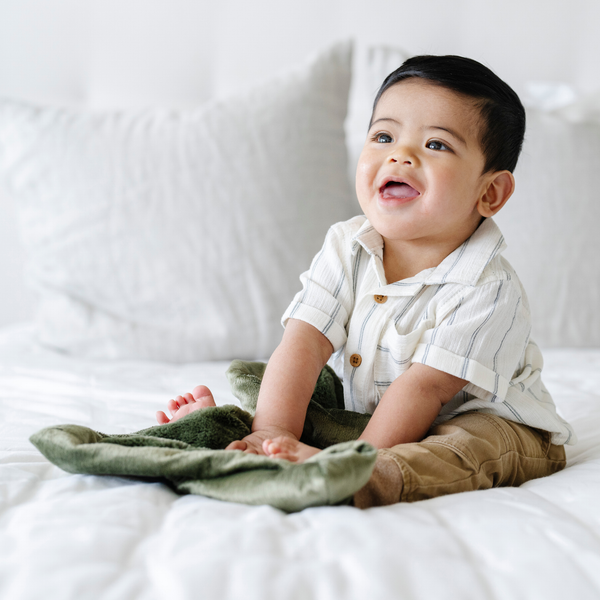 A baby boy holds a Mini Fern Colored Lush Saranoni Blanket. The soft blanket is a small blanket and a baby blanket.