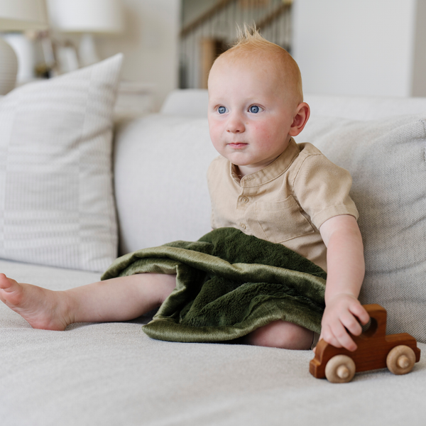 A baby boy sits with a Mini Fern Colored Lush Saranoni Blanket. The soft blanket is a small blanket and a baby blanket.