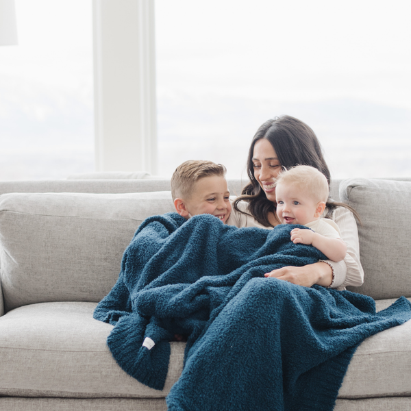 A mother and her kids sit with a Bamboni® blanket by Saranoni. This ultra-soft blanket is a blue blanket and made from a premium blend of bamboo rayon and poly microfiber, offering a lightweight, breathable, and fluffy feel. Perfect as a throw blanket, luxury blanket, plush throw, or soft blanket, it adds warmth and elegance to any living room, bedroom, or home décor setting. Designed for ultimate comfort, this buttery-soft Saranoni blanket is ideal for gifting. Enjoy this cozy blanket for years to come! 