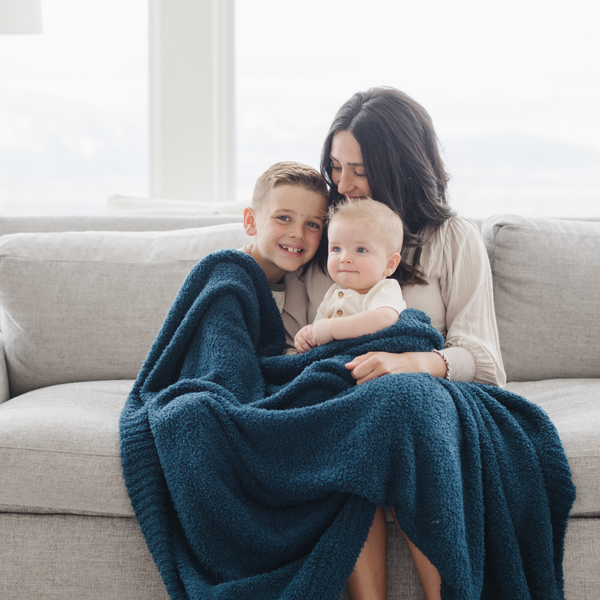 A mother and her kids sit with a Bamboni® blanket by Saranoni. This ultra-soft blanket is a blue blanket and made from a premium blend of bamboo rayon and poly microfiber, offering a lightweight, breathable, and fluffy feel. Perfect as a throw blanket, luxury blanket, plush throw, or soft blanket, it adds warmth and elegance to any living room, bedroom, or home décor setting. Designed for ultimate comfort, this buttery-soft Saranoni blanket is ideal for gifting. Enjoy this cozy blanket for years to come! 