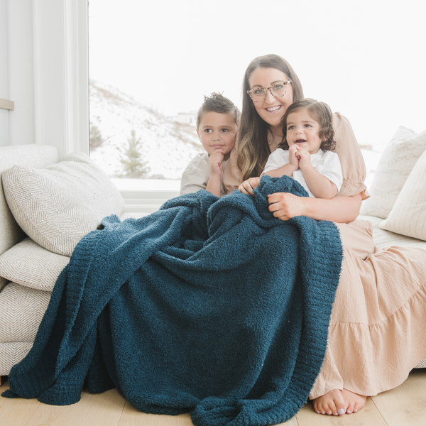 A mother and her son and daughter and a Bamboni® blanket by Saranoni. This ultra-soft blanket is a blue blanket and made from a premium blend of bamboo rayon and poly microfiber, offering a lightweight, breathable, and fluffy feel. Perfect as a extra large blanket, luxury blanket, or soft blanket, it adds warmth and elegance to any living room, bedroom, or home décor setting. Designed for ultimate comfort, this buttery-soft Saranoni blanket is ideal for gifting. Enjoy this cozy blanket for years to come! 