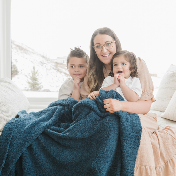 A mother and her kids sit with a Bamboni® blanket by Saranoni. This ultra-soft blanket is a blue blanket and made from a premium blend of bamboo rayon and poly microfiber, offering a lightweight, breathable, and fluffy feel. Perfect as a throw blanket, luxury blanket, plush throw, or soft blanket, it adds warmth and elegance to any living room, bedroom, or home décor setting. Designed for ultimate comfort, this buttery-soft Saranoni blanket is ideal for gifting. Enjoy this cozy blanket for years to come! 