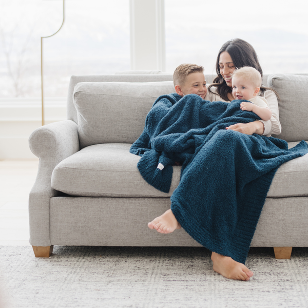 A mother and her kids sit under a Bamboni® blanket by Saranoni. This ultra-soft blanket is a blue blanket and made from a premium blend of bamboo rayon and poly microfiber, offering a lightweight, breathable, and fluffy feel. Perfect as a extra large blanket, luxury blanket, or soft blanket, it adds warmth and elegance to any living room, bedroom, or home décor setting. Designed for ultimate comfort, this buttery-soft Saranoni blanket is ideal for gifting. Enjoy this cozy blanket for years to come! 