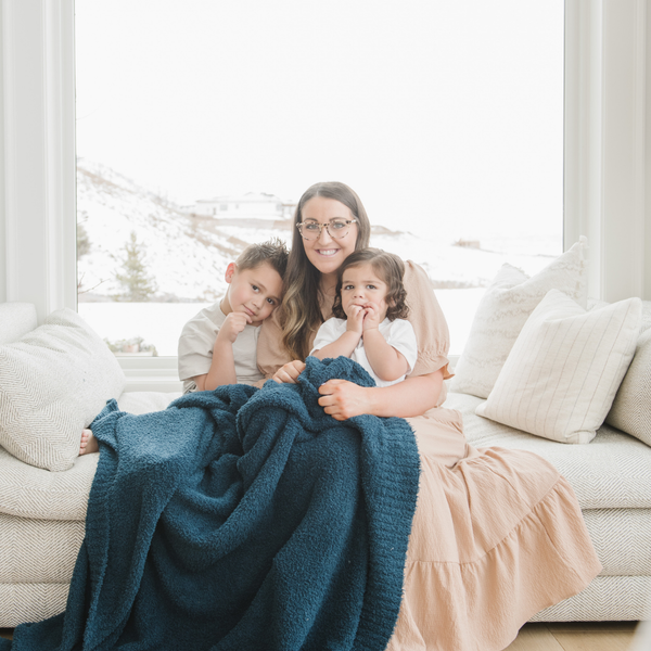 A mother and her kids sit with a Bamboni® blanket by Saranoni. This ultra-soft blanket is a blue blanket and made from a premium blend of bamboo rayon and poly microfiber, offering a lightweight, breathable, and fluffy feel. Perfect as a throw blanket, luxury blanket, plush throw, or soft blanket, it adds warmth and elegance to any living room, bedroom, or home décor setting. Designed for ultimate comfort, this buttery-soft Saranoni blanket is ideal for gifting. Enjoy this cozy blanket for years to come! 