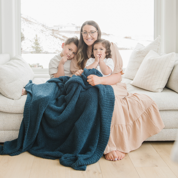 A mother and her little kids sit under a Bamboni® blanket by Saranoni. This ultra-soft blanket is a blue blanket and made from a premium blend of bamboo rayon and poly microfiber, offering a lightweight, breathable, and fluffy feel. Perfect as a extra large blanket, luxury blanket, or soft blanket, it adds warmth and elegance to any living room, bedroom, or home décor setting. Designed for ultimate comfort, this buttery-soft Saranoni blanket is ideal for gifting. Enjoy this cozy blanket for years to come! 