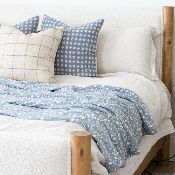 A blue and white Saranoni XL muslin quilt in a soft floral print is draped on a bed. This luxury blanket features four layers of ultra-soft bamboo muslin, creating an airy yet cozy feel. Designed with a stitched quilted pattern and a one-inch border, this breathable blanket is perfect for muslin lovers looking for extra warmth and comfort. Made from bamboo fabric, this soft muslin quilt is a lightweight quilt that offers a cozy, home décor accent. The softest blanket and a Saranoni blanket. 