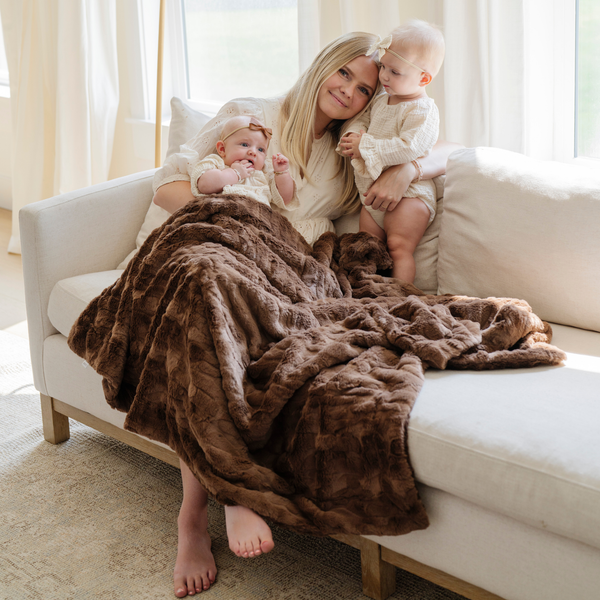 A woman and her two little girls have a brown luxurious patterned faux fur throw blanket that is a Saranoni blanket. This ultra-soft, plush throw blanket adds a touch of elegance and warmth to any space, perfect as a soft throw blanket or fluffy blanket for lounging. Ideal for those seeking a high-quality artificial fur blanket or luxury blanket, this versatile and stylish soft blanket enhances both comfort and decor. Shop the best blankets and throws for ultimate relaxation and cozy vibes.