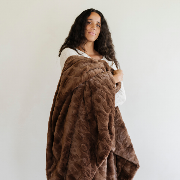 A woman holds a brown luxurious patterned faux fur throw blanket that is a Saranoni blanket. This ultra-soft, plush throw blanket adds a touch of elegance and warmth to any space, perfect as a soft throw blanket or fluffy blanket for lounging. Ideal for those seeking a high-quality artificial fur blanket or luxury blanket, this versatile and stylish soft blanket enhances both comfort and decor. Shop the best blankets and throws for ultimate relaxation and cozy vibes.