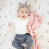 A baby girl is laying down and holding a peach blanket that is a Bamboni® blanket, offering ultimate softness and warmth. Made from Saranoni’s signature stretchy, cloud-like Bamboni® fabric, this luxury baby blanket provides comfort for naps, tummy time, and on-the-go snuggles. The soft blanket is a mini blanket and Saranoni blanket. 