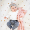 A baby girl that is laying down is holding a peach blanket that is a Bamboni® blanket, offering ultimate softness and warmth. Made from Saranoni’s signature stretchy, cloud-like Bamboni® fabric, this luxury baby blanket provides comfort for naps, tummy time, and on-the-go snuggles. The soft blanket is a mini blanket and Saranoni blanket. 