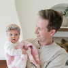 A father holds his baby girl and a double-layer Bamboni® baby blanket. The plush, breathable blanket features a two-tone light pink and pink floral design, offering ultimate softness and warmth. Made from Saranoni’s signature stretchy, cloud-like Bamboni® fabric, this luxury baby blanket provides comfort for naps, tummy time, and on-the-go snuggles. The soft blanket is a mini blanket and Saranoni blanket. 