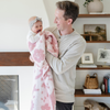 A father smiles and holds his baby girl who is holding a double-layer Bamboni® blanket. The plush, breathable blanket features a two-tone light pink and pink floral design, offering ultimate softness and warmth. Made from Saranoni’s signature stretchy, cloud-like Bamboni® fabric, this luxury kids blanket provides comfort for naps and on-the-go snuggles. The soft blanket is a toddler blanket and Saranoni blanket. 