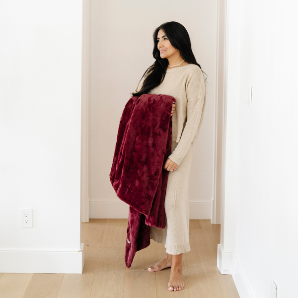 A woman holds a pomegranate luxurious patterned faux fur throw blanket that is a Saranoni blanket. This ultra-soft, plush throw blanket adds a touch of elegance and warmth to any space, perfect as a soft throw blanket or fluffy blanket for lounging. Ideal for those seeking a high-quality artificial fur blanket or luxury blanket, this versatile and stylish soft blanket enhances both comfort and decor. Shop the best blankets and throws for ultimate relaxation and cozy vibes.