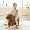 A joyful little boy toddler with curly hair smiles while riding a plush brown dog rocker. Dressed in a stylish striped outfit, the child is seated in a bright, airy room adorned with plants and a cozy rug, showcasing the perfect blend of playful decor and comfort. Ideal for parents looking for engaging and plush toys for their children's playrooms.