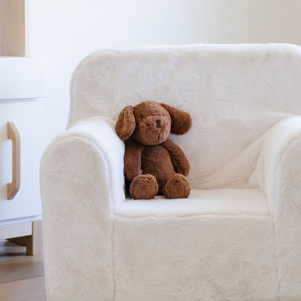 A cozy white plush chair is adorned with a soft brown stuffed dog sitting comfortably on the seat. This inviting scene showcases stylish children's furniture, perfect for creating a warm and playful atmosphere in a child's room. Ideal for parents searching for comfortable seating options paired with adorable plush toys, this setup highlights the perfect combination of style and comfort.