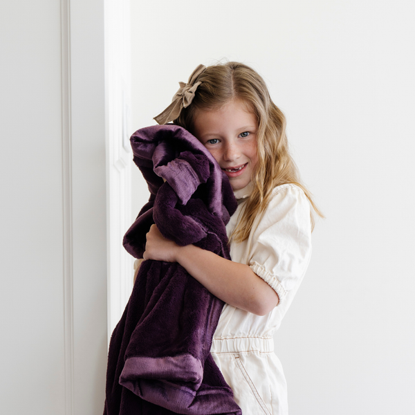 A little girl holds a Receiving Aubergine (deep purple) Colored Lush Saranoni Blanket. The soft blanket is a small blanket and a baby blanket or toddler blanket.