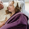 A father holds his little girl who is sitting with a Aubergine (deep purple) Colored Lush Saranoni Blanket draped over her. The soft blanket is a small blanket and a baby blanket or toddler blanket.