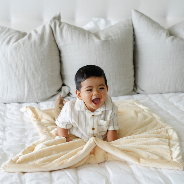 A baby boy lays on a Receiving Chiffon (light yellow) Colored Lush Saranoni Blanket. The soft blanket is a small blanket and a baby blanket or toddler blanket.