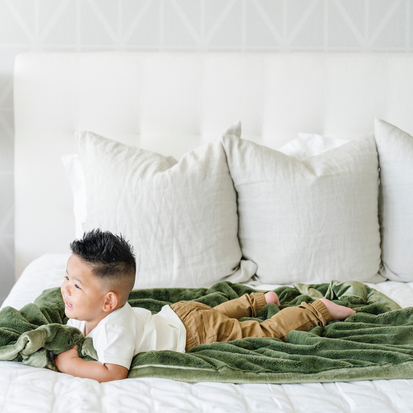 A little boy lays on a Receiving Fern Colored Lush Saranoni Blanket. The soft blanket is a small blanket and a baby blanket or toddler blanket.