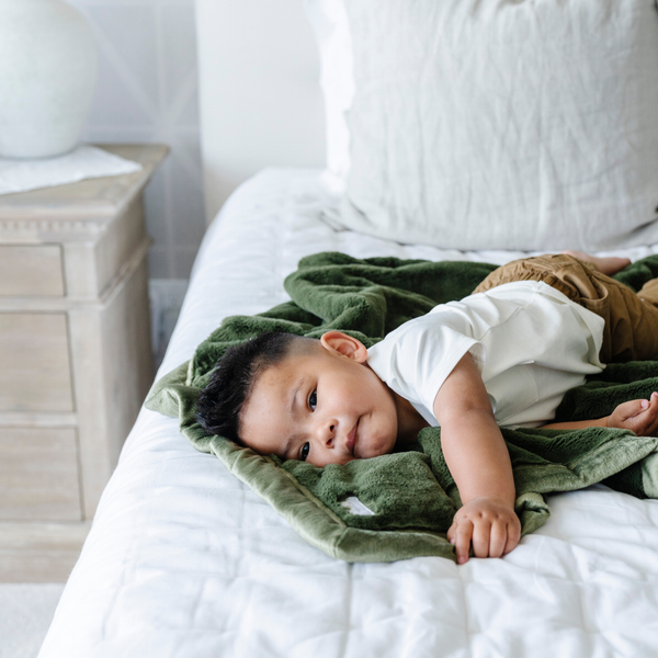 A little boy lays on a Receiving Fern Colored Lush Saranoni Blanket. The soft blanket is a small blanket and a baby blanket or toddler blanket.