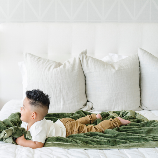 A little boy lays on a Receiving Fern Colored Lush Saranoni Blanket. The soft blanket is a small blanket and a baby blanket or toddler blanket.