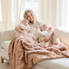 A mother and her two daughters sit with a rouge colored extra large patterned faux fur throw Saranoni Luxury Blanket. The soft blanket is an oversized throw blanket.