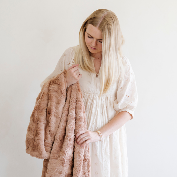 A woman holds a rouge luxurious patterned faux fur throw blanket that is a Saranoni blanket. This ultra-soft, plush throw blanket adds a touch of elegance and warmth to any space, perfect as a soft throw blanket or fluffy blanket for lounging. Ideal for those seeking a high-quality artificial fur blanket or luxury blanket, this versatile and stylish soft blanket enhances both comfort and decor. Shop the best blankets and throws for ultimate relaxation and cozy vibes.