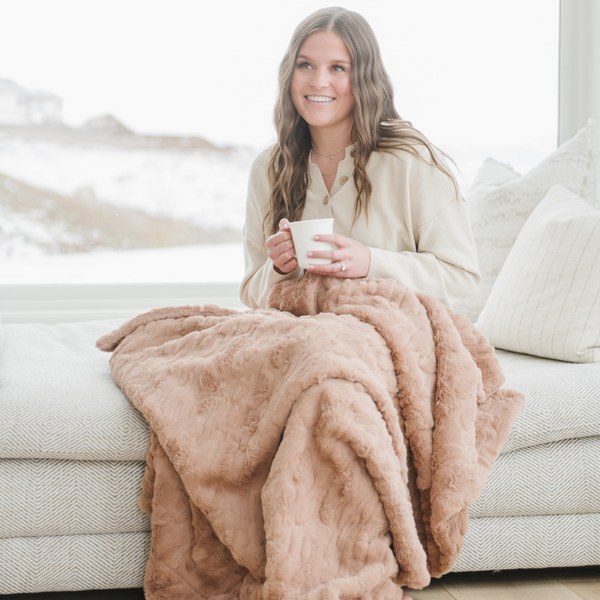 A woman sits with a rouge luxurious patterned faux fur throw blanket that is a Saranoni blanket. This ultra-soft, plush throw blanket adds a touch of elegance and warmth to any space, perfect as a soft throw blanket or fluffy blanket for lounging. Ideal for those seeking a high-quality artificial fur blanket or luxury blanket, this versatile and stylish soft blanket enhances both comfort and decor. Shop the best blankets and throws for ultimate relaxation and cozy vibes.