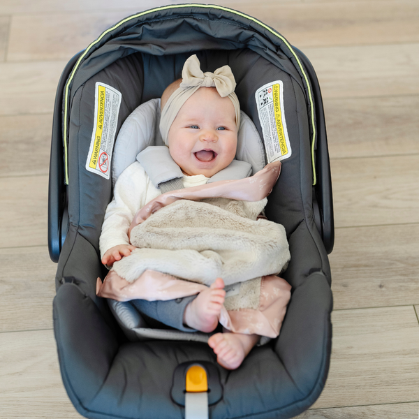 A happy baby girl and a satin back blanket. The lush blanket is tan with a peach satin border that has a floral design on it. The satin back blanket is a lush blanket with a satin border and back. The soft blanket is a luxury blanket and a Saranoni blanket. This mini blanket is an adorable baby blanket and perfect for littles. 