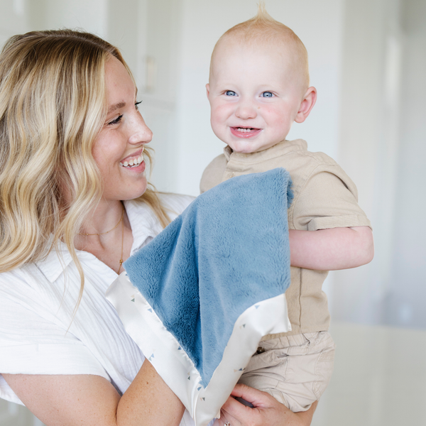 Mom and son happily snuggled up with a blue and white satin bordered mini blanket.