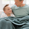 A father and son sit with a Bamboni® blanket by Saranoni. This ultra-soft blanket is a light blue blanket and made from a premium blend of bamboo rayon and poly microfiber, offering a lightweight, breathable, and fluffy feel. Perfect as a extra large blanket, luxury blanket, or soft blanket, it adds warmth and elegance to any living room, bedroom, or home décor setting. Designed for ultimate comfort, this buttery-soft Saranoni blanket is ideal for gifting. Enjoy this cozy blanket for years to come!