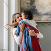 A mother plays with her little boy while holding a receiving blanket with a Superman™ icon on it. The soft blanket is light blue and red. This kids blanket is a luxury blanket and a Saranoni blanket. The blanket is also a double-layer Bamboni® blanket. 