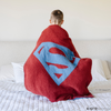 A little boy holds a receiving blanket with a Superman™ icon on it. The soft blanket is light blue and red. This kids blanket is a luxury blanket and a Saranoni blanket. The blanket is also a double-layer Bamboni® blanket. 